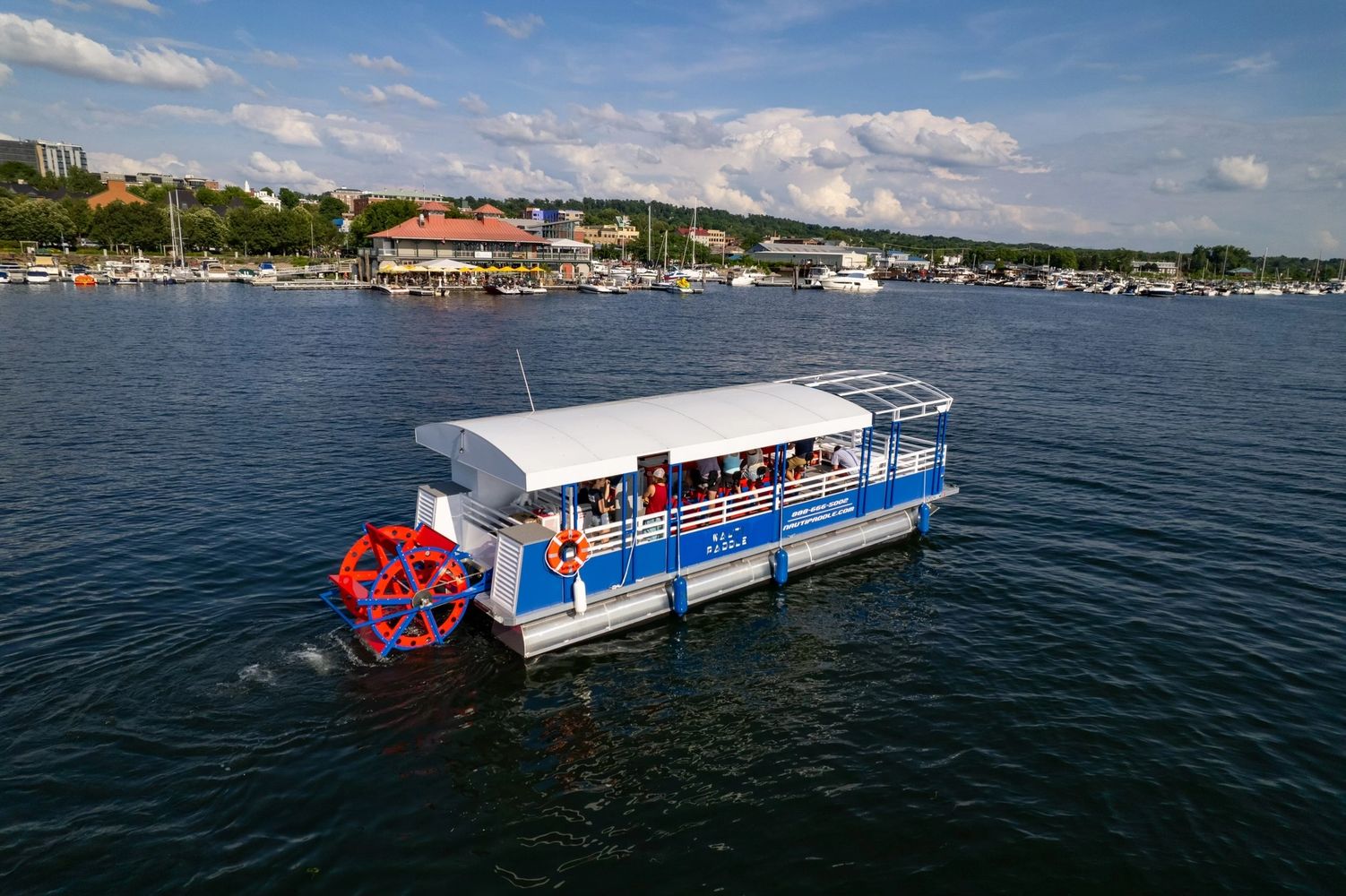 A blue and white paddle boat cruising on a lake with passengers.