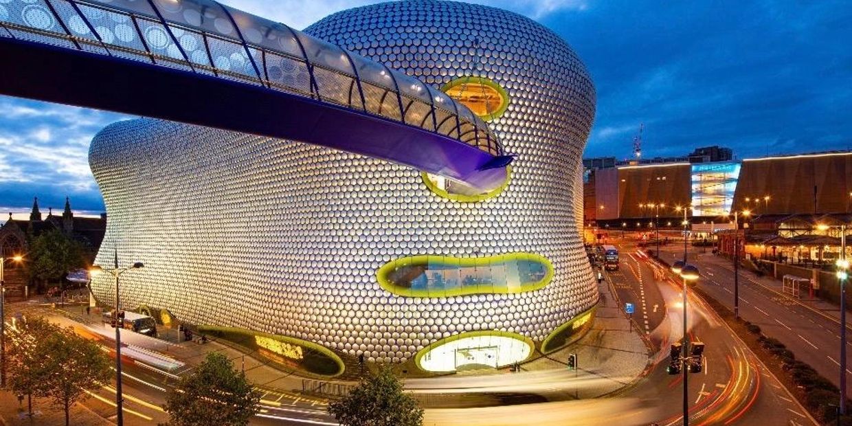 Futuristic building with curved design and a glass skybridge at dusk.