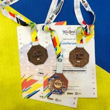 Three medals and certificates from the 2025 Taekwondo Championship are displayed on a blue and yellow mat.