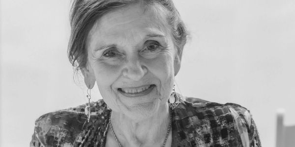 Elderly woman smiling warmly, holding a plastic cup.
