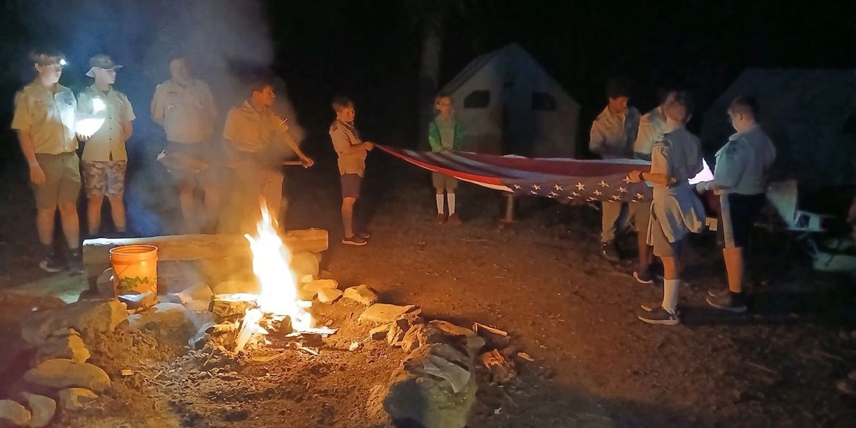 Group of scouts performing a flag ceremony by the campfire at night.