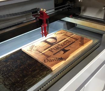 Laser engraving a wooden board with names and design elements.
