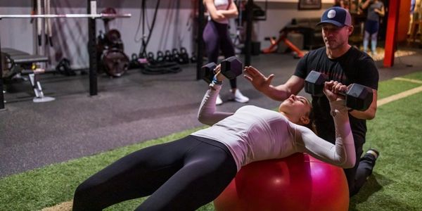 Personal trainer spotting female client performing ball dumbbell chest press.