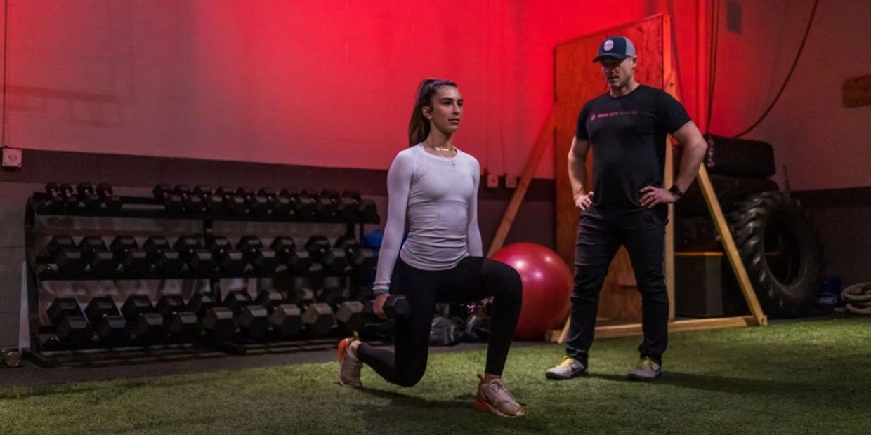 Personal trainer teaching lunge exercise to female client.