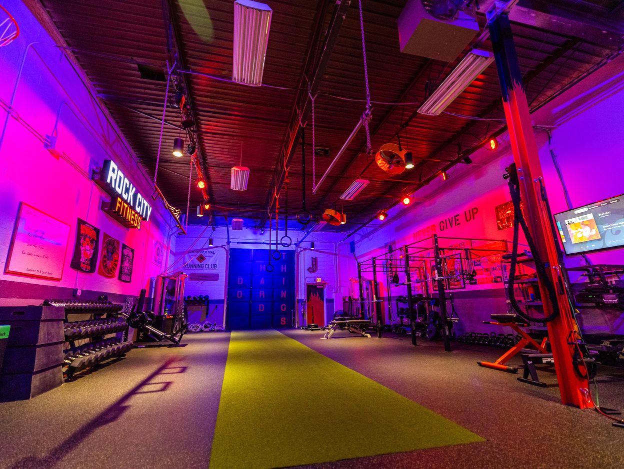 Vibrantly lit Rock City Fitness gym with workout equipment and motivational signs.