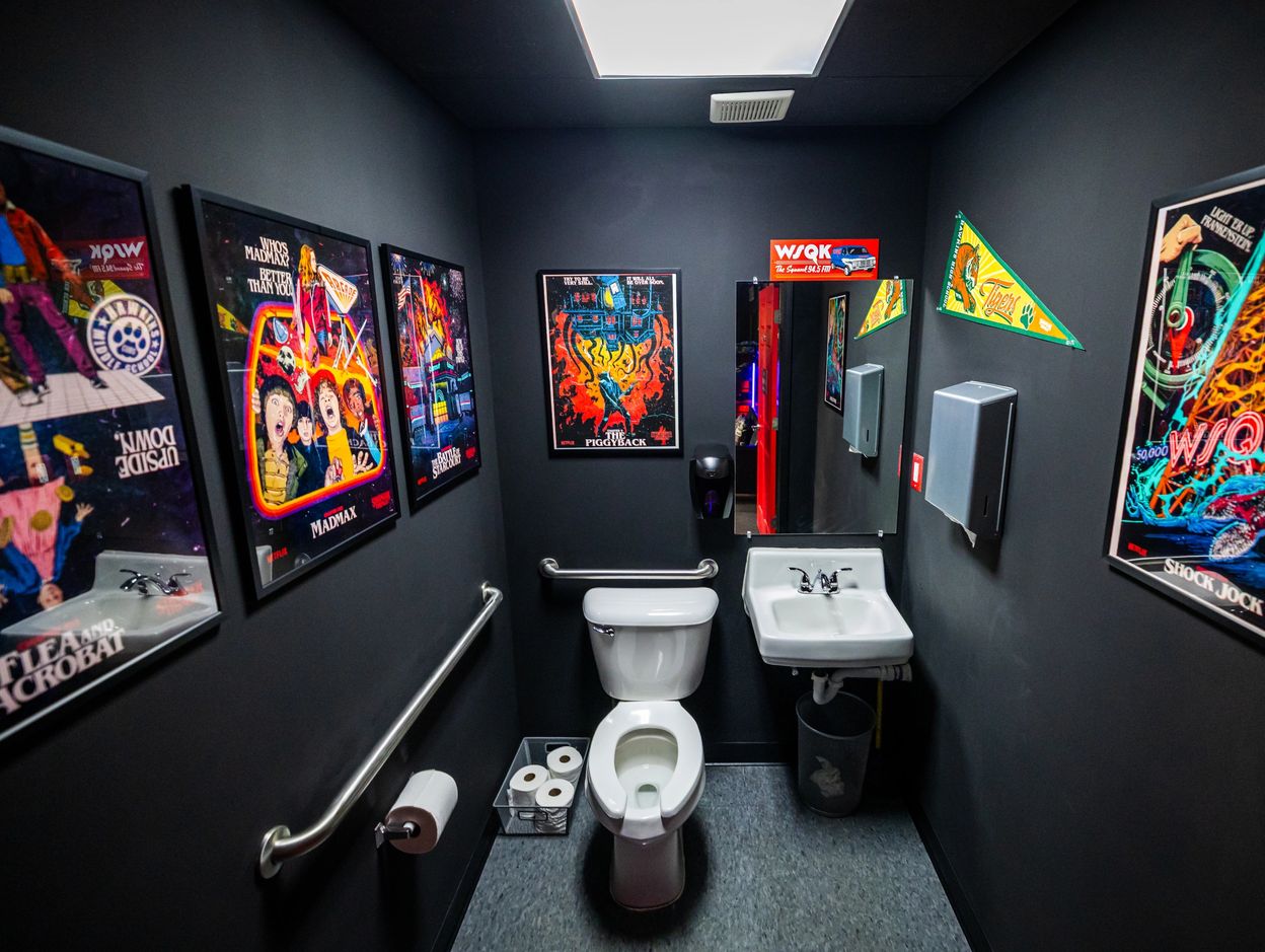 A vibrant, retro-themed bathroom with colorful posters and a small sink next to a toilet.
