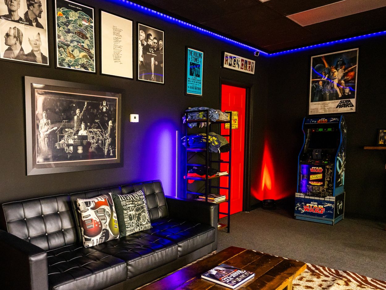 Cozy entertainment room with music posters, gaming arcade, and stylish black sofa.