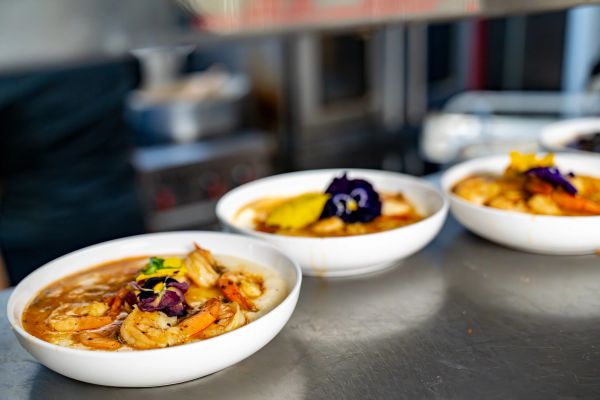 Three bowls of shrimp and grits garnished with edible flowers on a kitchen counter.