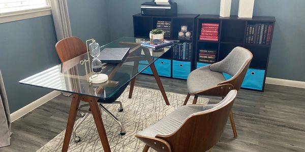 Glass desk with two chairs on one side, and one wooden chair the other