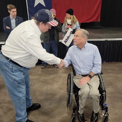 Person in a wheelchair shaking hands with a man in a US flag cap.
