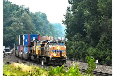 A freight train with colorful containers traveling through a green forested area.