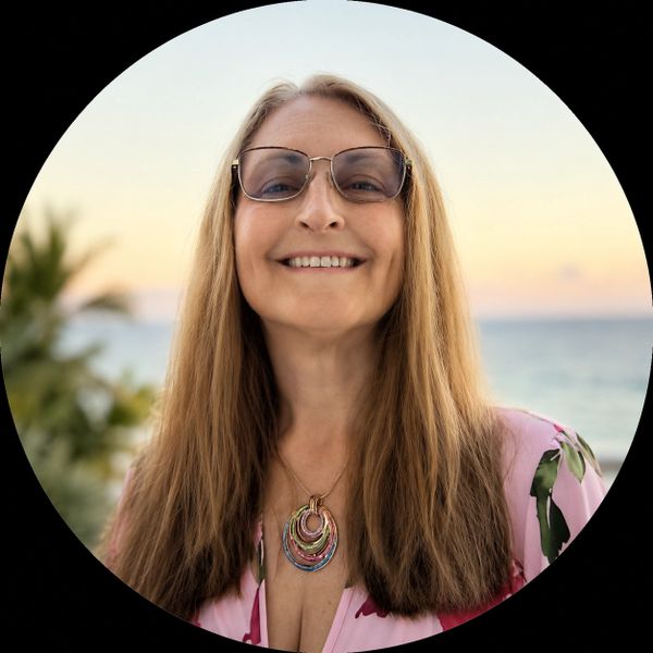 Smiling woman with long hair and glasses by the beach at sunset.