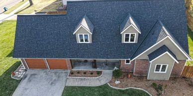 A modern house with a dark shingle roof and two dormer windows.