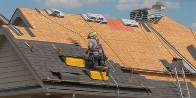 A roofer installing shingles on a house under construction.
