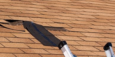 A roof with damaged shingles and a ladder nearby.