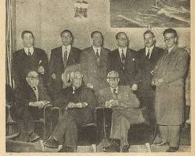 A vintage black-and-white group photo of nine men in suits and coats.