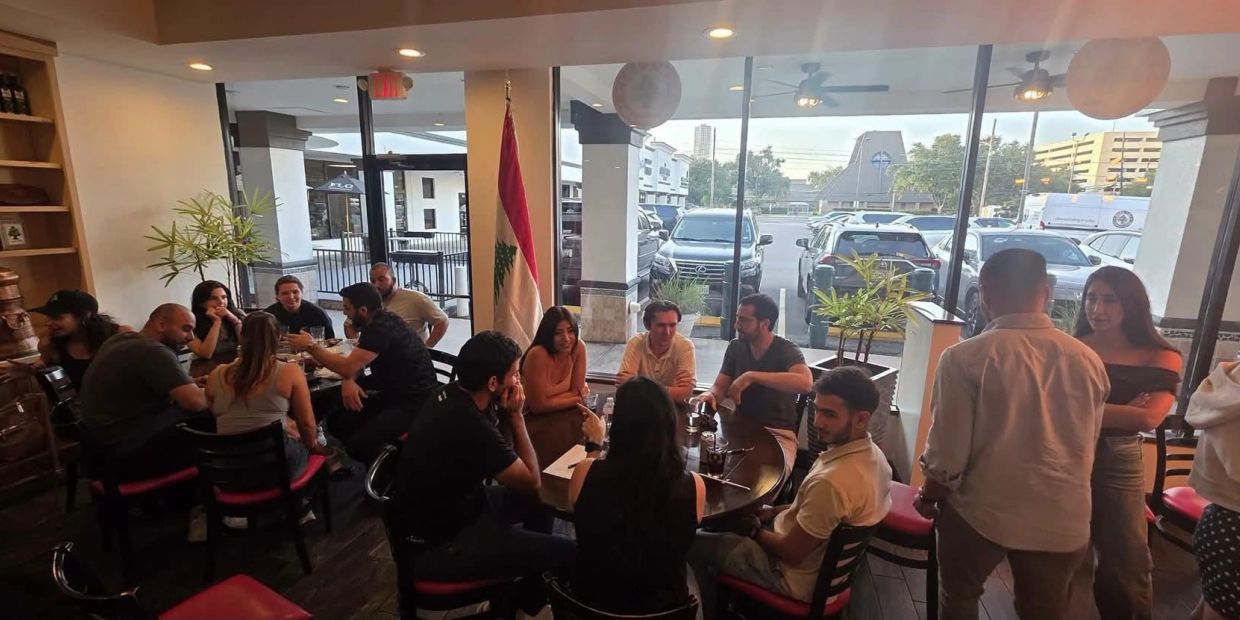 Group of people socializing inside a restaurant with a Lebanese flag.
