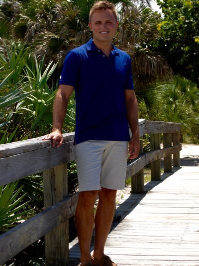 Man in blue shirt and beige shorts on a wooden boardwalk.