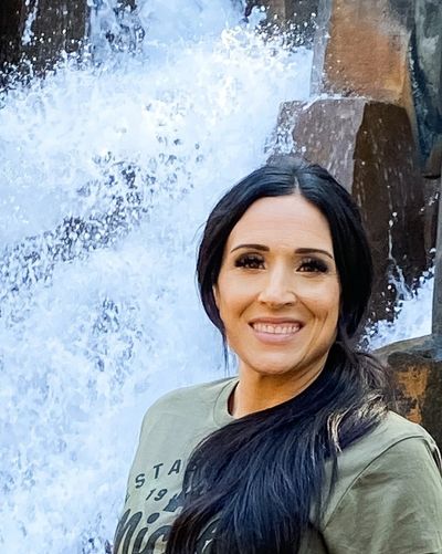 Smiling woman with long hair by a waterfall.