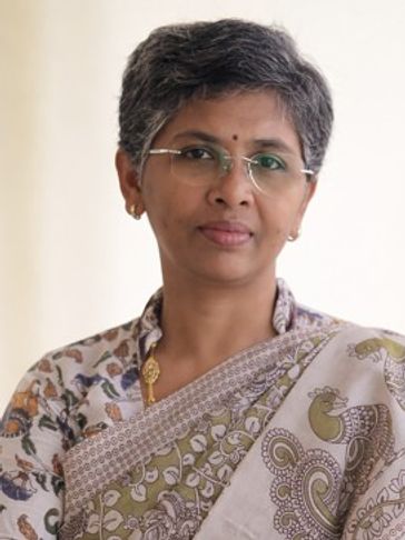 A woman in a patterned sari with glasses and short hair.