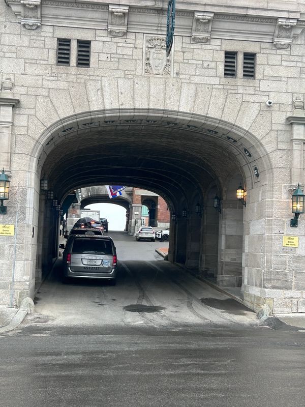Stone archway tunnel with cars passing through under a cloudy sky.