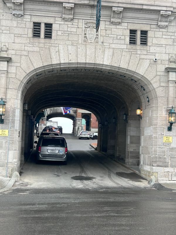 Cars passing through a historic stone archway on a sloped road.