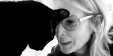 A woman and a black cat share a close moment.