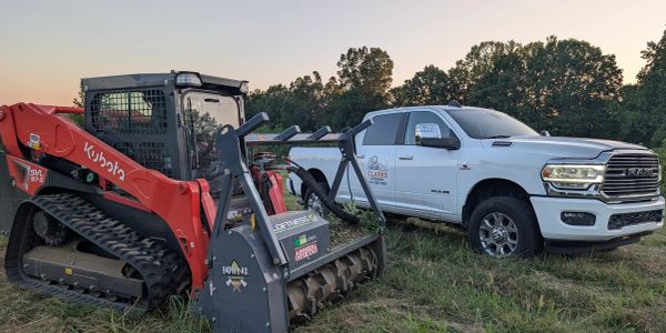White RAM truck and Kubota excavator in a field.