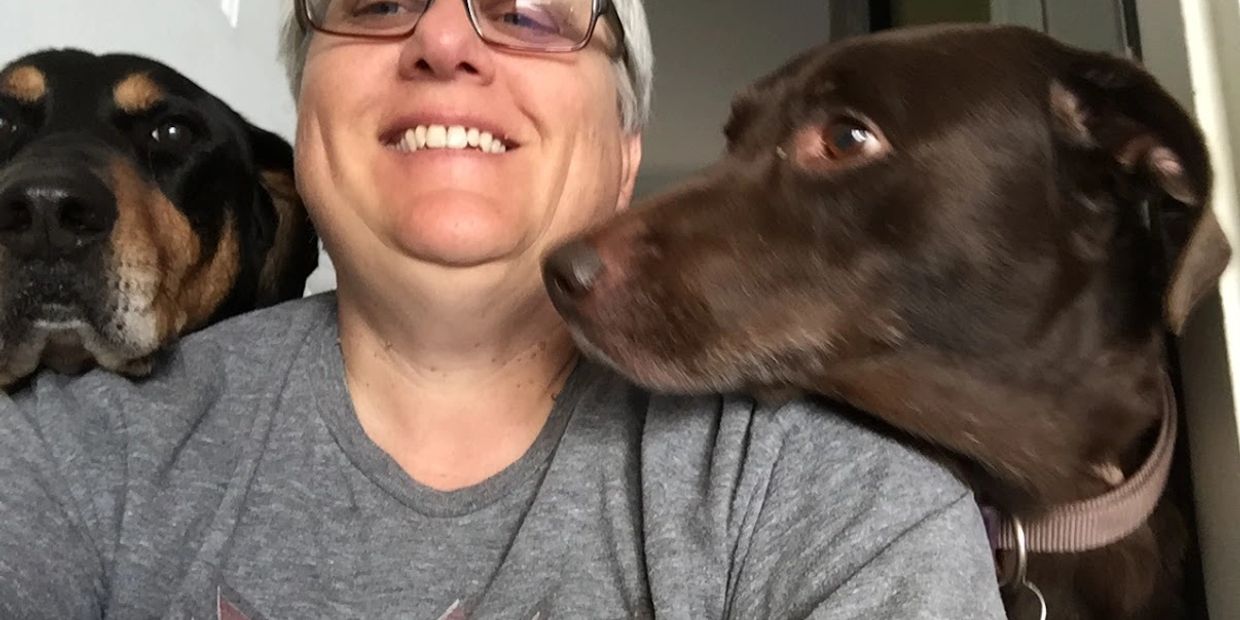 Smiling person with two dogs close by, sharing a warm moment indoors.