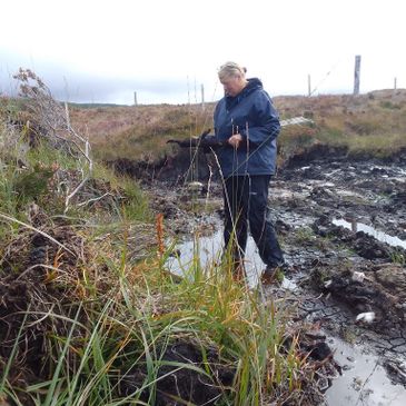 Person in raincoat exploring muddy outdoor area with tall grass.