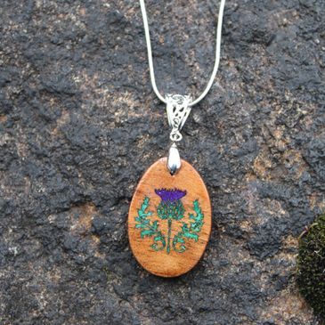 Oval wooden pendant with a purple thistle flower design on a silver chain.