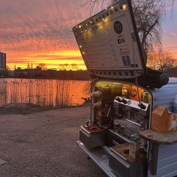 Mobile coffee stall at sunset by a lake with a colorful sky.