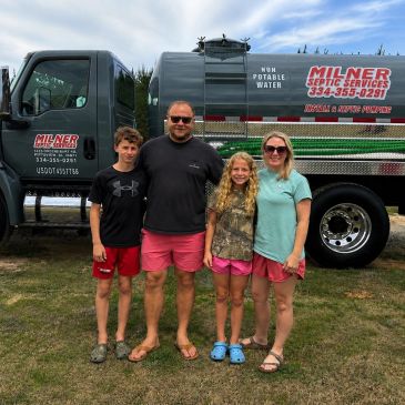 Family of four standing in front of a septic service truck.