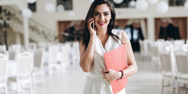Confident woman in white holding a folder and talking on phone in a bright room.