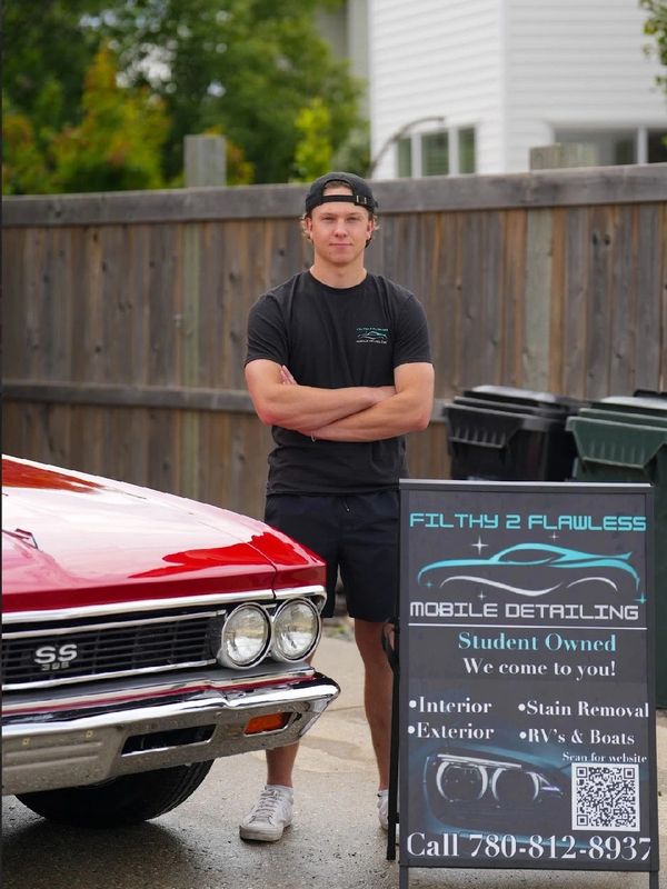 Young man standing by a red classic car and mobile detailing sign.