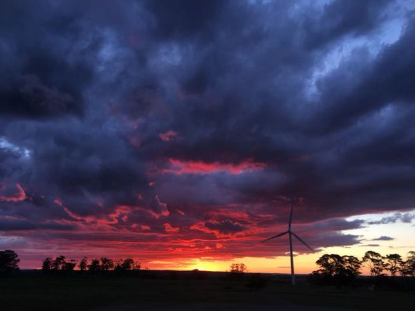 Dramatic sunset with dark clouds and a wind turbine silhouette.