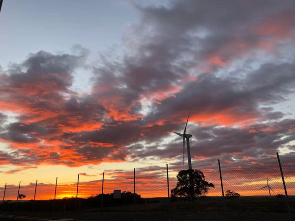Wind turbines silhouetted against a vibrant sunset sky with dramatic clouds.