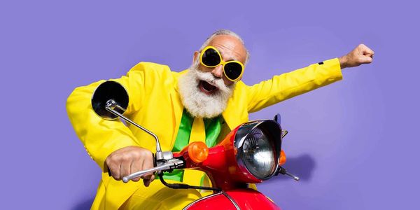 Energetic elderly man in bright yellow suit riding a red scooter, striking a fun pose.