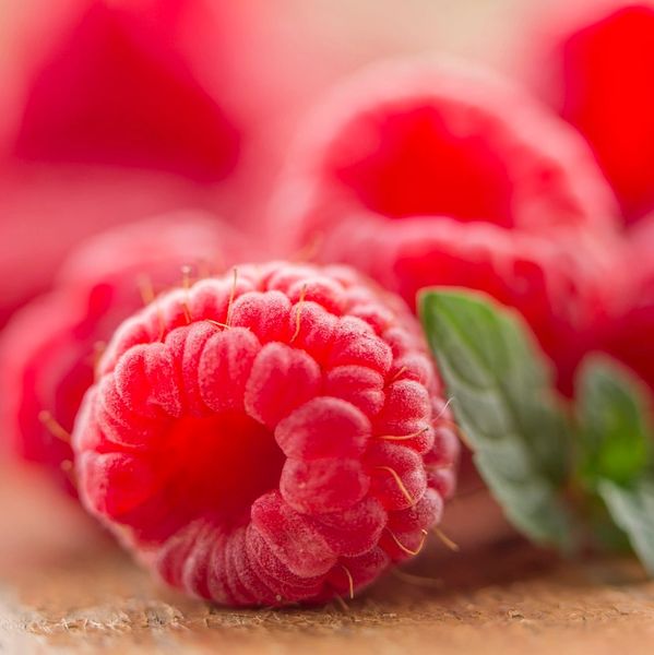 Close-up of fresh red raspberries with a green leaf on a wooden surface.