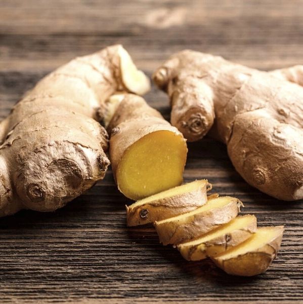 Fresh ginger roots and sliced ginger on wooden surface.