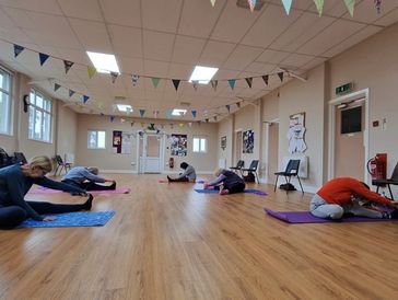 Group stretching on mats in a decorated community hall with wooden floors.