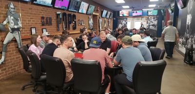 Group of people playing poker in a lively game room with sports decor.