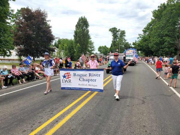 People march in a parade holding a Rogue River Chapter banner in Rockford, Michigan.