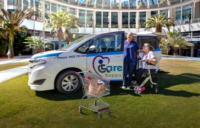 Caregiver assisting elderly woman using walker near care support vehicle.