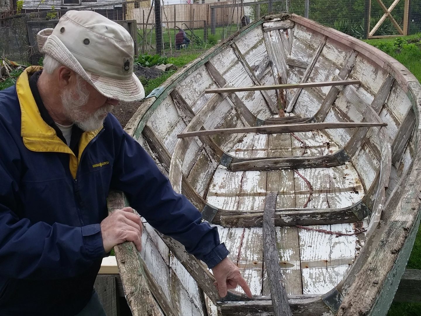 An elderly man examines an old, weathered wooden boat outdoors.