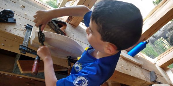 Boatshop camper shaping a model boat using traditional hand tools.