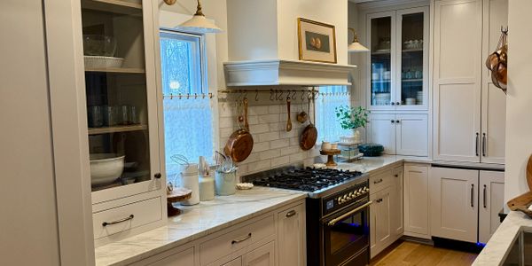 Cozy kitchen with white cabinets, marble countertops, and copper pans hanging by the stove.