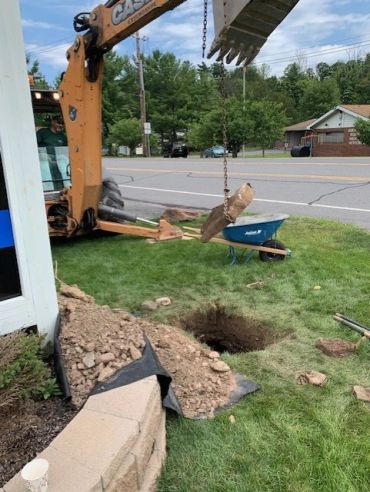 Excavator digging a hole near a building on a grassy area.