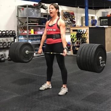Woman deadlifting heavy barbell in gym.