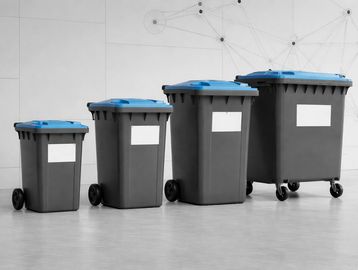 Four grey waste bins with blue lids of varying sizes lined up indoors.
